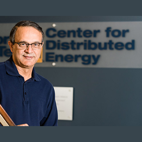 Deepak Divan, Director of the Center for Distributed Energy, stands in front of the CDE sign outside their offices.