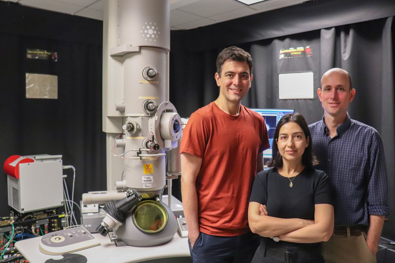 A photo of Vida Jamali, assistant professor the School of Chemical and Biomolecular Engineering; Amirali Aghazadeh, assistant professor in the School of Electrical and Computer Engineering; and Josh Kacher, associate professor in the School of Materials Science and Engineering standing in front of a TEM at Georgia Tech. Photo Courtesy of Amelia Neumeister; Georgia Tech