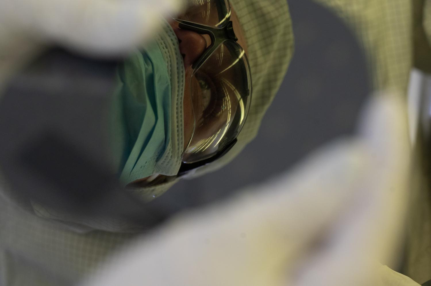 Close-up of a person wearing protective goggles and a face mask, inspecting a circular wafer inside a cleanroom environment.