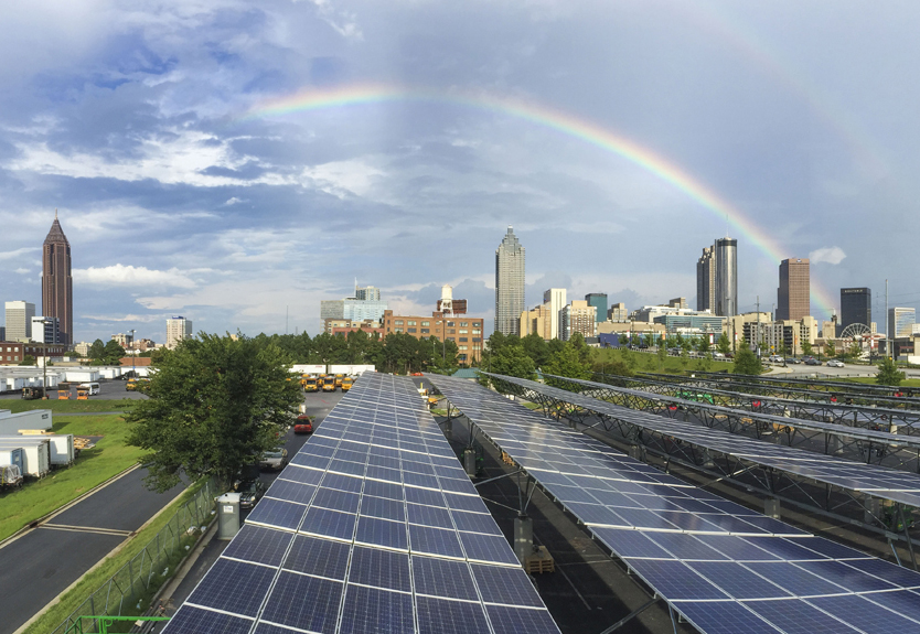 An improbably composition of a solar panel array against the backdrop of the Alanta skyline  with a double rainbow as a background.