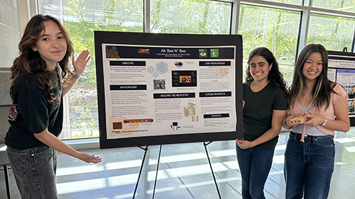 Three female students gather around their academic poster to present their research in the atrium of one of Georgia Tech's buildings.