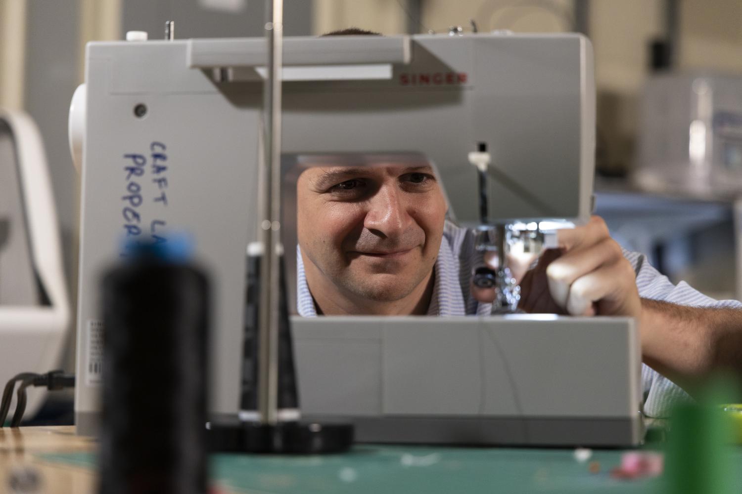 Close-up of a sewing machine on a worktable with thread spools in the foreground, as someone adjusts the machine during a crafting process.