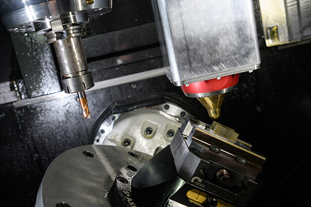 Close-up view of advanced manufacturing equipment, showing a CNC machine with a drill bit and a laser head positioned near a metal workpiece.