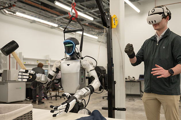 Person wearing a virtual reality headset controlling a humanoid robot equipped with tools in a laboratory setting.