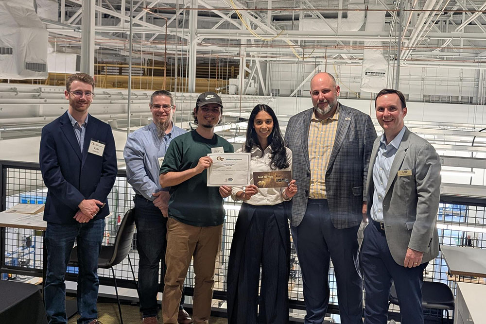 Group of individuals standing indoors holding a certificate and plaque, posing in front of an industrial facility setting.