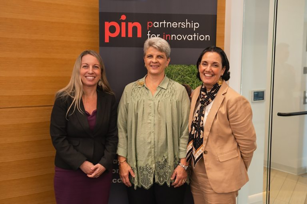 Three people standing together in front of a ‘Partnership for Innovation’ event banner.