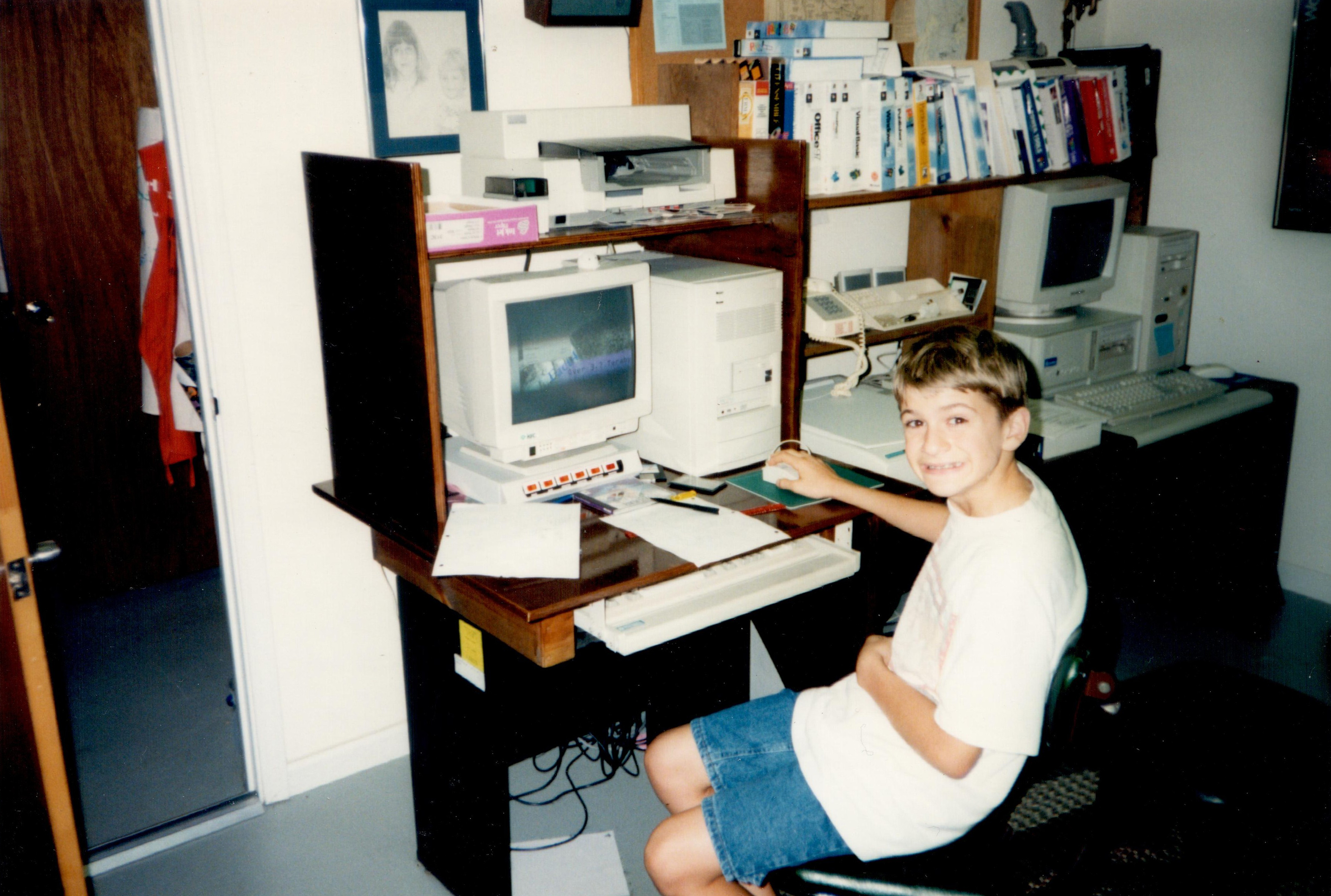 young boy sitting at a desk while working on a late 1990s computer