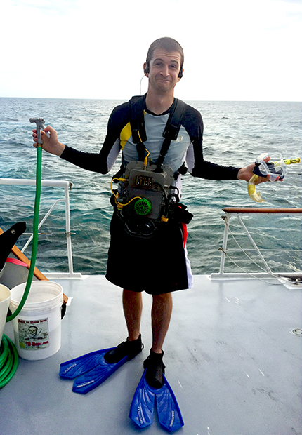 man wearing foot flippers standing on a boat with the ocean behind him