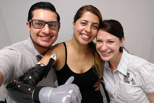 Three people posing closely together, with one person wearing a prosthetic arm featuring a sleek black and silver design.