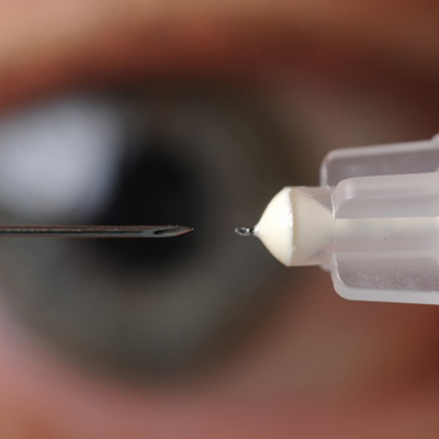 Close-up of a microneedle and applicator approaching the surface of an eye for precise drug delivery.
