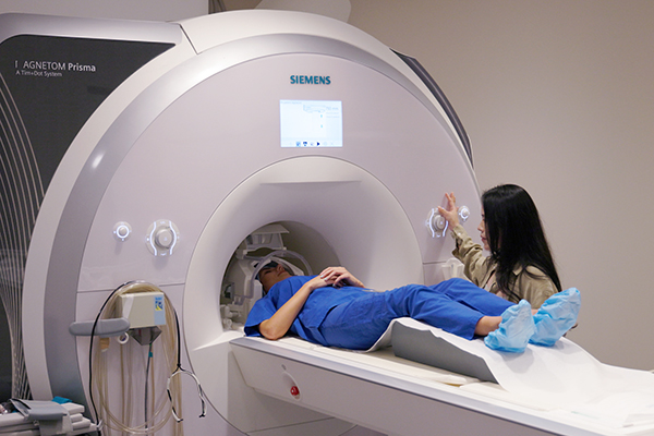 Yiren Ren standing next to an MRI as a research participant is about the have the memory area of the brain scanned.