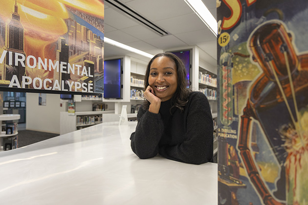Person seated at a white table in a library, with colorful posters featuring science fiction and environmental themes in the foreground.