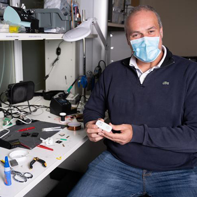 Omer Inan sitting at his desk with electronics parts surrounding him.