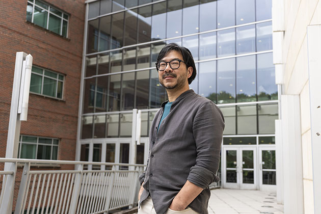 Man wearing glasses in a gray shirt standing in front of a building with many windows