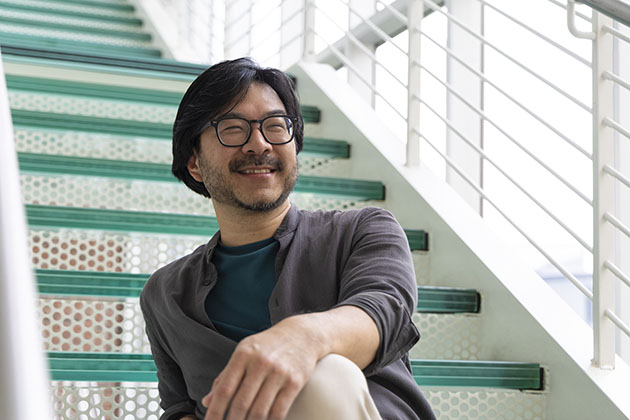 Man wearing glasses in a gray shirt sitting on green-tinted glass stairs