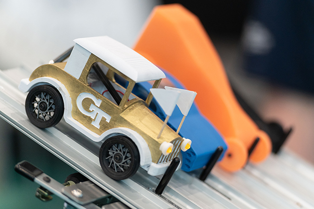Close-up of small, colorful model race cars lined up on a track, including a gold-and-white car with “GT” on the side.