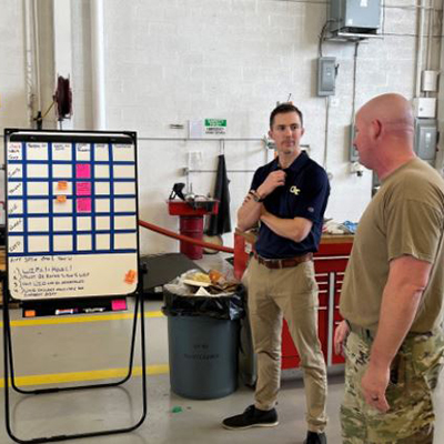 Two people standing in a workspace, discussing data displayed on a large monitor.
