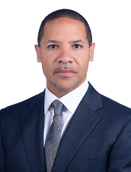 Person in a dark suit and patterned tie posing against a plain white background