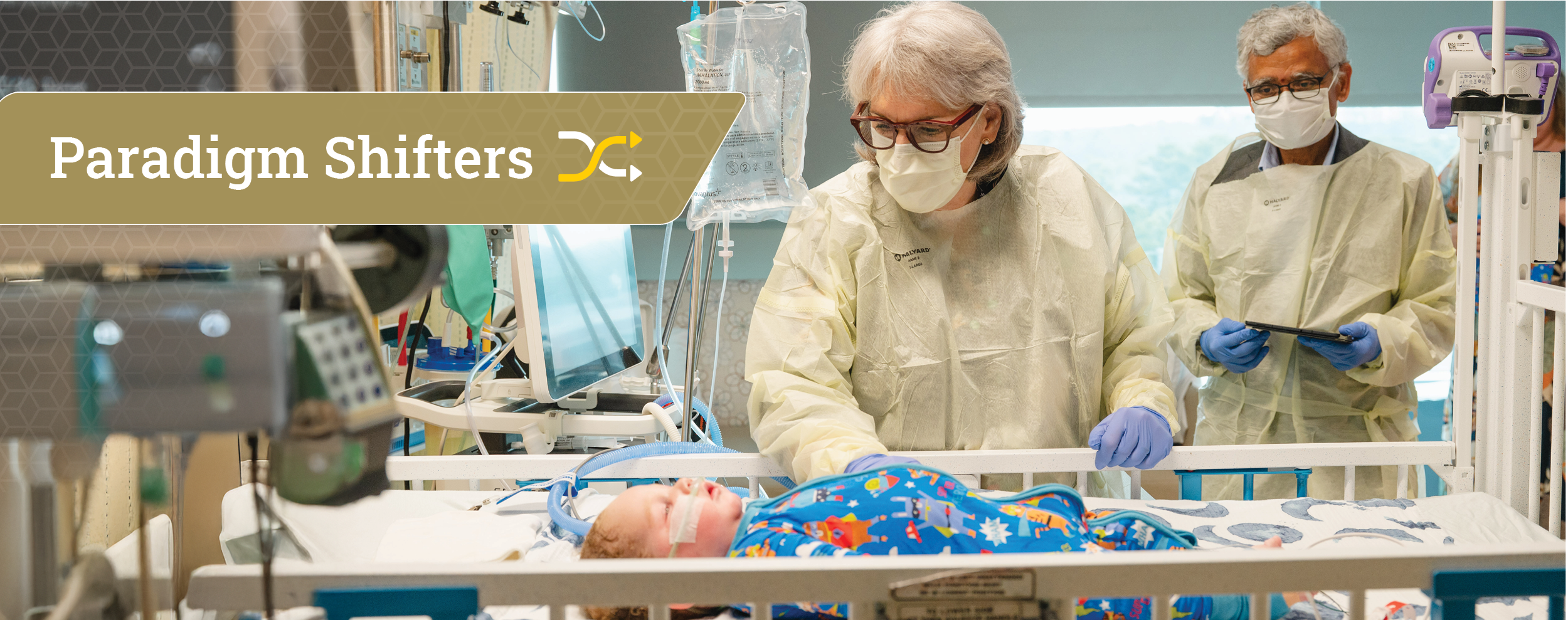 Two masked healthcare professionals in protective gowns attend to an infant in a hospital crib beside a gold 'Paradigm Shifters' banner with a stylized arrow logo.