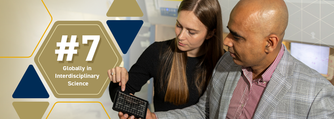 Two individuals collaborating on a project, one pointing at a small electronic device with a keypad, alongside a graphic displaying '#7 Globally in Interdisciplinary Science' with geometric shapes in blue, gold, and gray.