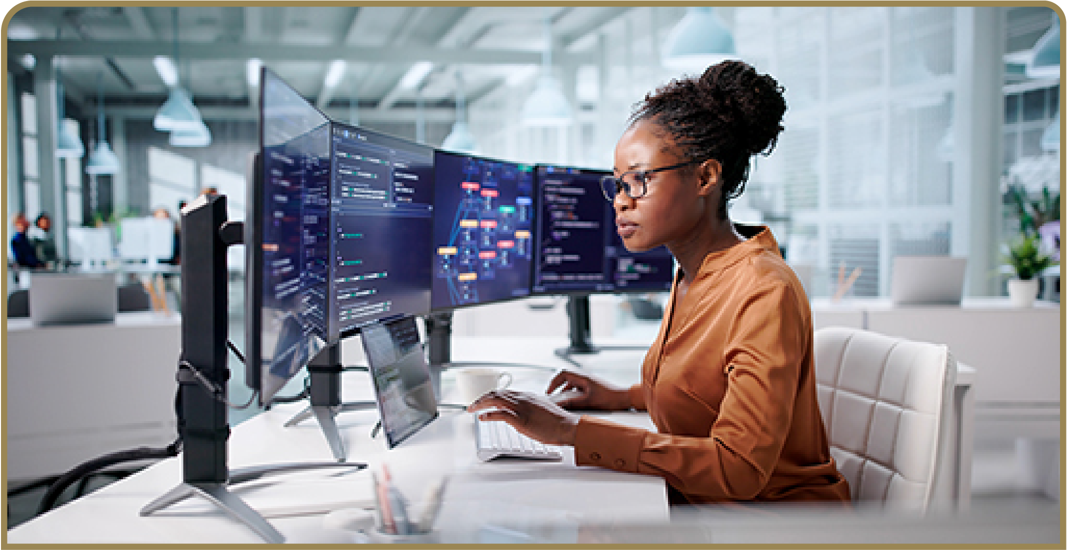 Person works at a multi-monitor computer workstation displaying software code and data in a modern office.