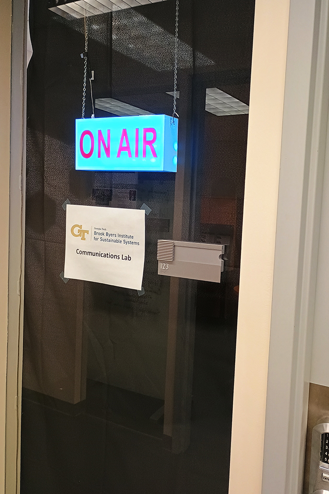 A backlit "On Air" sign hangs inside the window to the BBISS Communications Lab.