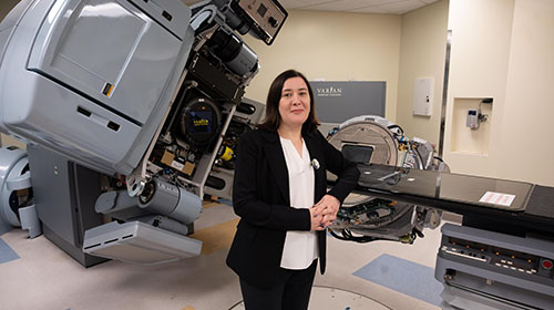 female standing in a Georgia Tech lab with a large piece of gray equipment in the background