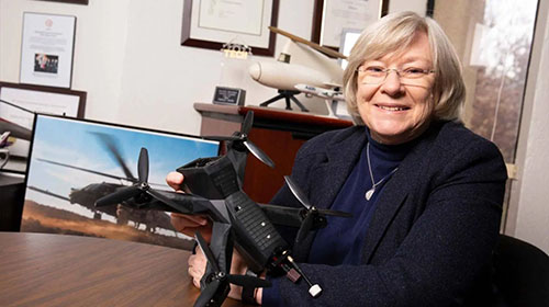 female sitting at a desk in an office holding a model rotorcraft