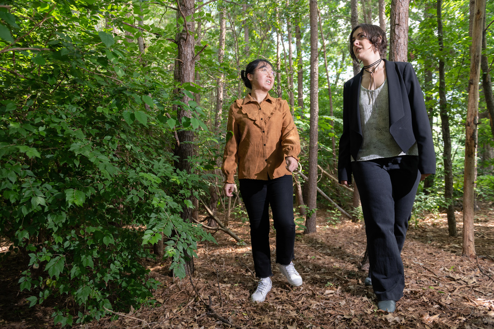 Two women walk and talk together along a path in the woods.