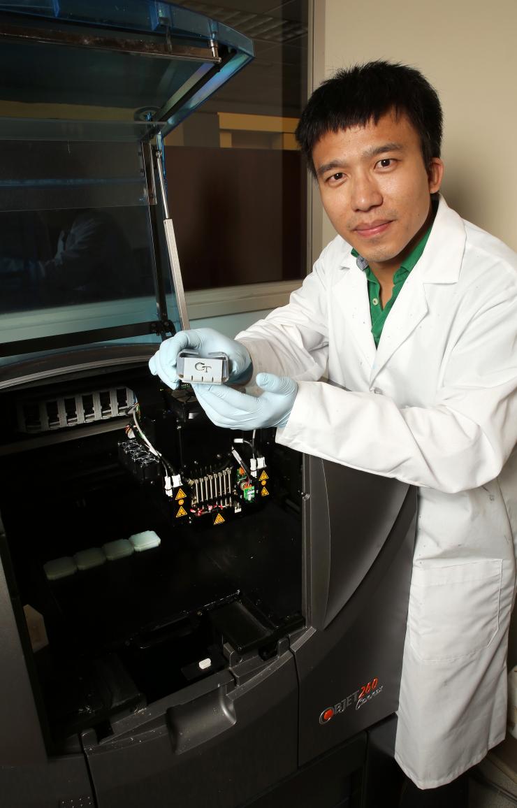 <p>Yiqi Mao, a postdoctoral fellow in the laboratory of Professor Jerry Qi at Georgia Tech, shows a folded box structure produced from smart shape-memory materials. The materials were created with the 3-D printer shown with him. (Credit: Candler Hobbs, Georgia Tech)</p>