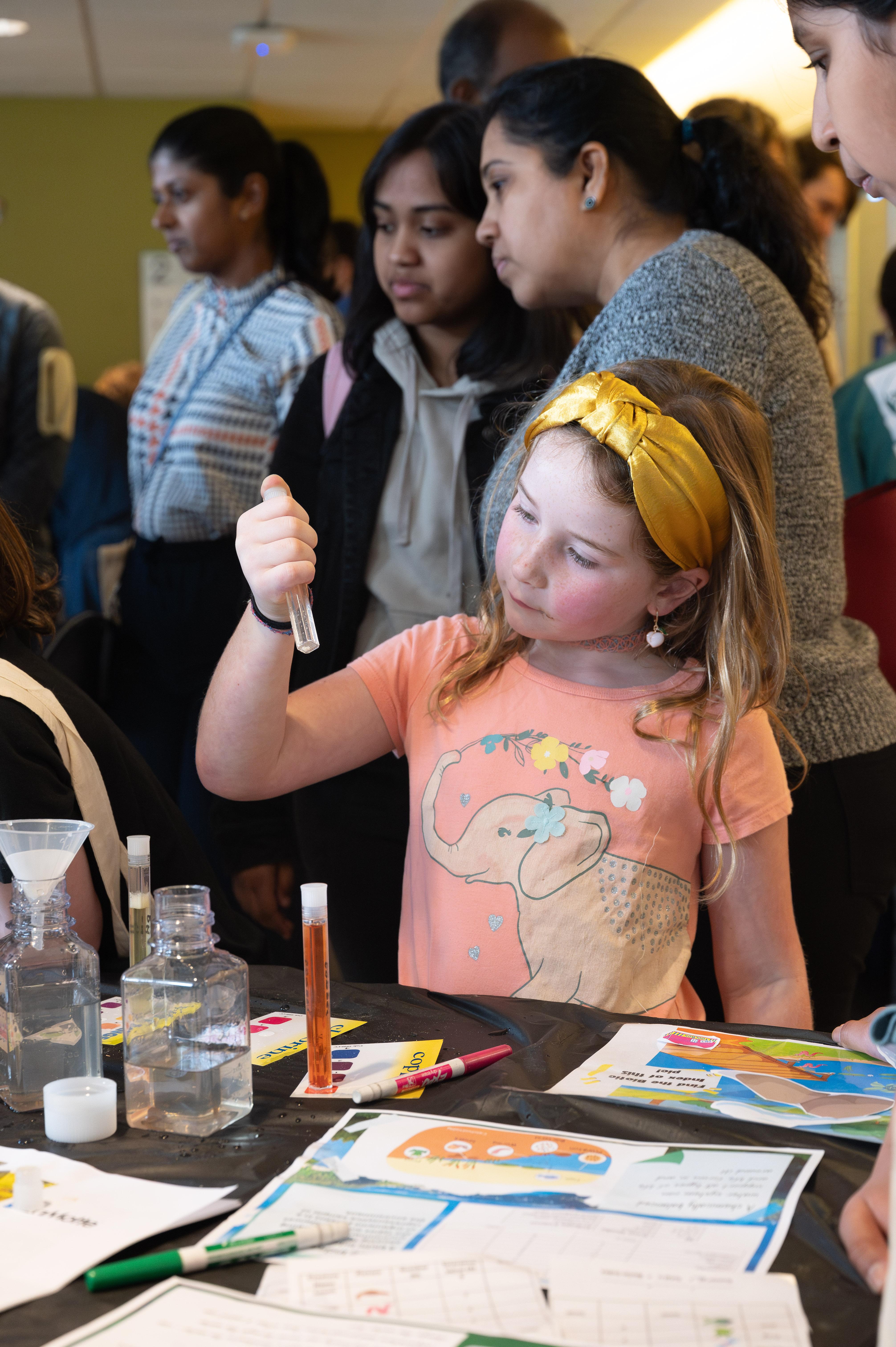Little girl in yellow headband examines a test tube. 