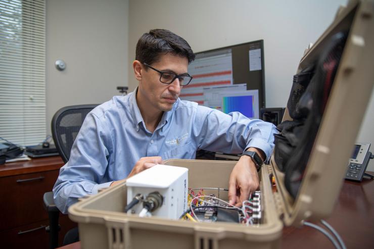 <p>GTRI Senior Research Engineer Aharon Karon (left) and Research Engineer Aprameya Satish prepare to place an infrasound detection device under a small wind cover during a field test. (Credit: Christopher Moore, GTRI).</p>