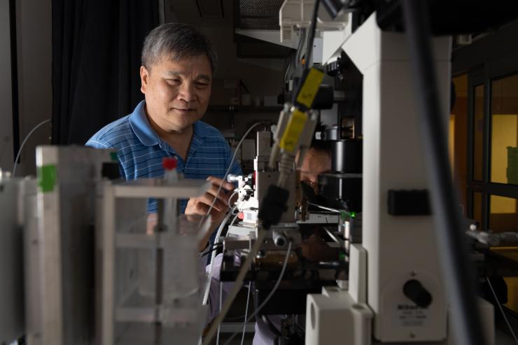 <p>Cheng Zhu in his lab at Georgia Tech stands over a microscope station set up to observe forces researchers exert and measure on structures of living cells. Georgia Tech / Allison Carter</p>