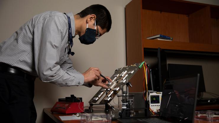 <p>GTRI senior research scientist Nicholas Guise tests the electronics on a microchip that will be used to grow DNA strands for archival storage of data. (Credit: Sean McNeil, GTRI)</p>