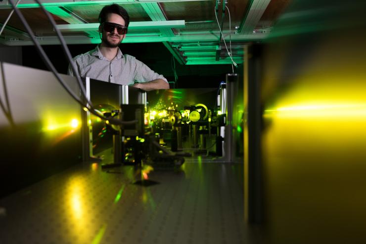 <p>Georgia Tech graduate research assistant Felix Thouin in Carlos Silva's lab stands at a table where laser light in the visible range undergoes processing to ready it for use in measuring materials qualities. Credit: Georgia Tech / Allison Carter</p>