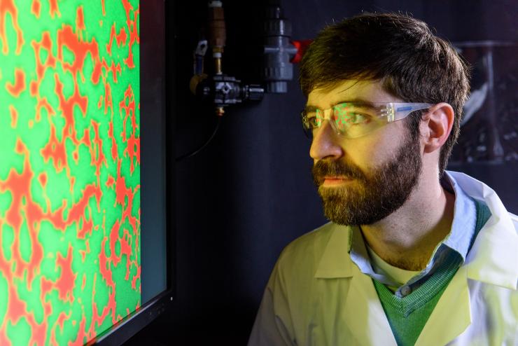<p>Principal investigator Peter Yunker in a photo for an unrelated experiment. Here, Yunker is looking at an image for a study on changes in territorial divisions caused by dueling strains of cholera bacteria. Credit: Rob Felt / Georgia Tech</p>