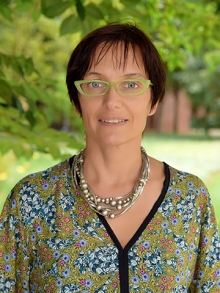 A woman with short brown hair and green glasses in front of a tree