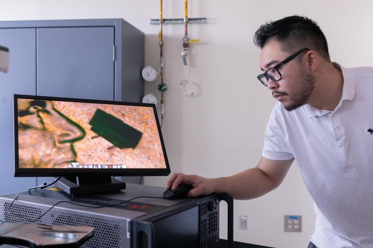 <p>Georgia Tech graduate student Zhijian (Chris) Hao is shown with a microscope image of a micro-bristle-bot on a U.S. penny. (Photo: Allison Carter, Georgia Tech)</p>