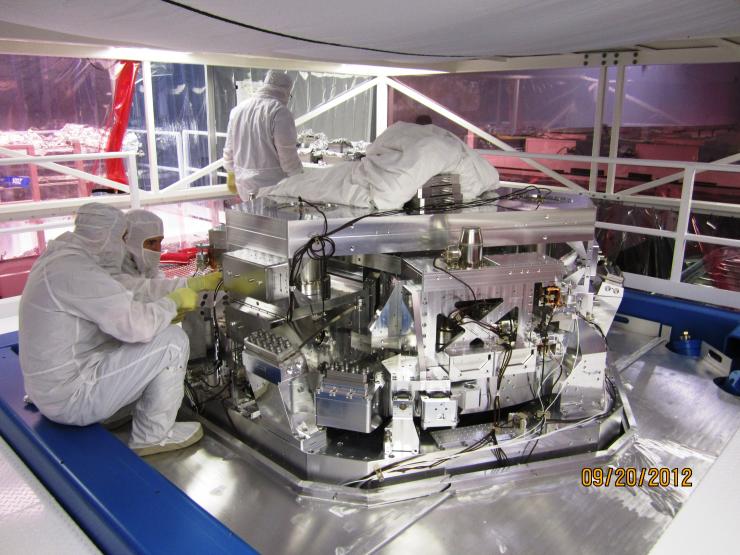 <p>Workers in Livingston, Louisiana are shown installing equipment used to split a powerful laser into two beams, each one traveling down a different arm of the LIGO observatory. The beams bounce off a mirror at the end of each arm and return to the center exactly out of phase, cancelling out the energies of each. (Credit: LIGO Scientific Collaboration)</p>