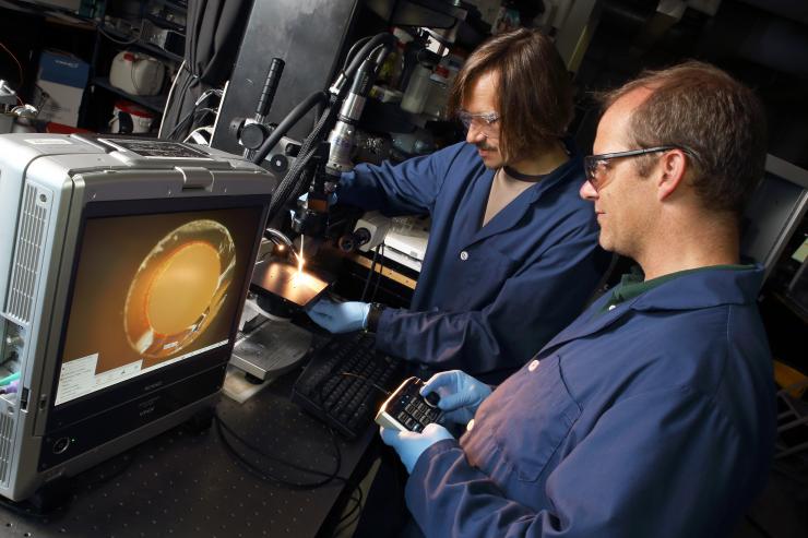 <p>Georgia Tech professor Andrei Fedorov (left) and senior research engineer Peter Kottke adjust the optics on a study of how hydrogel coatings affect capillary action in a narrow glass tube. (Credit: Candler Hobbs, Georgia Tech)</p>