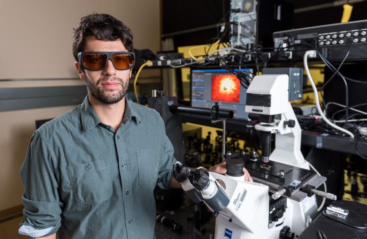<p>Sean Rodrigues, a Ph.D. candidate in the Georgia Tech School of Electrical and Computer Engineering, is shown with equipment used to study a chiral metamaterial whose properties in the nonlinear regime produce a significant spectral shift with power levels in the milliwatt range. (Credit: Rob Felt, Georgia Tech)</p>