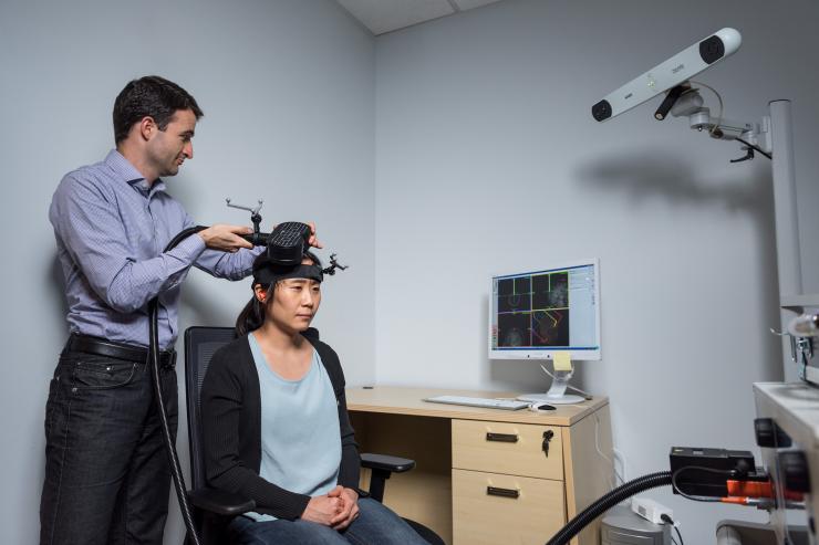 <p>Researcher Dobromir Rahnev demonstrates the application of transcranial magnetic stimulation (TMS) in a Georgia Tech psychology research center with graduate student Ji-Won Jung. Credit: Georgia Tech / Rob Felt</p>
