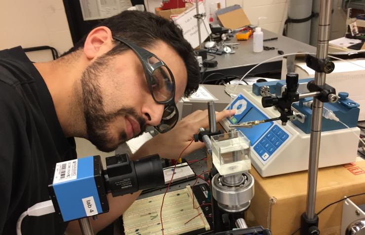 <p>Georgia Tech Ph.D. candidate Alexandros Fragkopoulos adjusts equipment used to create unstable toroidal droplets in viscous silicone oil. The droplets are part of a study to understand how the droplets evolve into spherical forms. (Credit: John Toon, Georgia Tech)</p>
