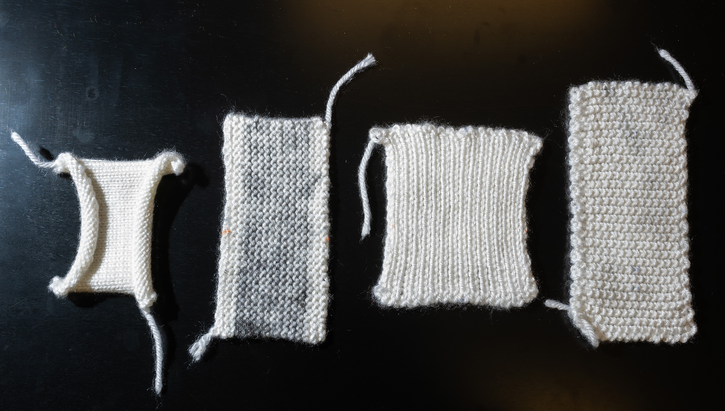 Four small samples of white fabric on a black background. 
