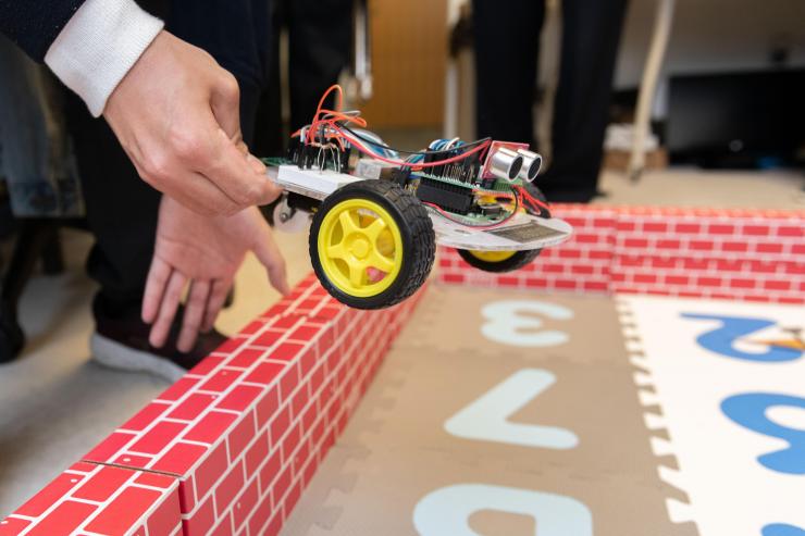 <p>Georgia Tech Researcher Ningyuan Cao places a robotic car controlled by an ultra-low power hybrid chip into a test arena where it will demonstrate its ability to learn and collaborate with another robot. (Photo: Allison Carter, Georgia Tech)</p>