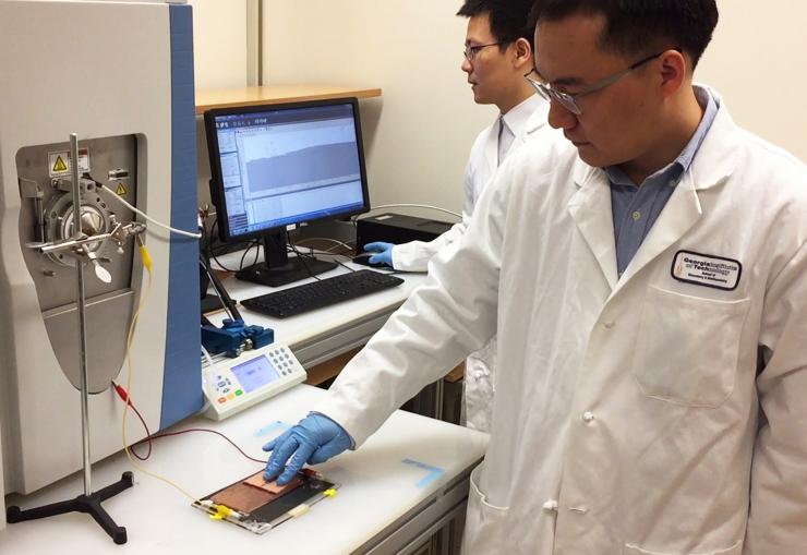 <p>Anyin Li, a postdoctoral fellow in the School of Chemistry and Biochemistry, actuates a triboelectric nanogenerator (foreground) while Yunlong Zi, a postdoctoral fellow in the School of Materials Science and Engineering, observes the spectra generated by the charged particles. (Credit: John Toon, Georgia Tech)</p>