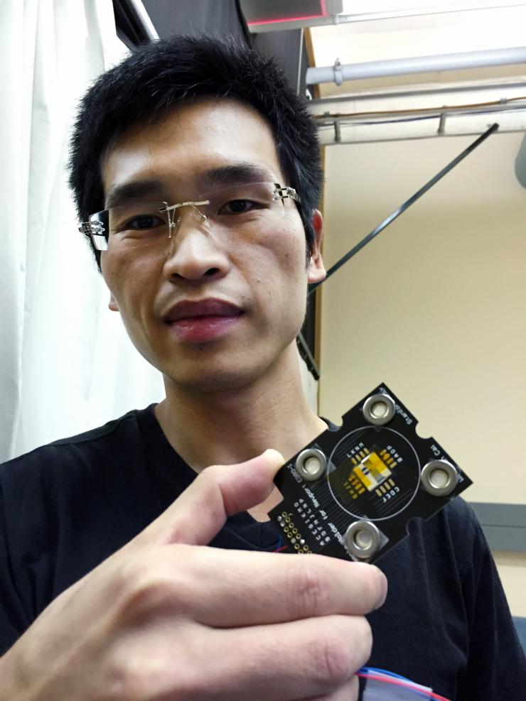 <p>Georgia Tech graduate student Shoufeng Lan holds a metamaterial waveguide located at the center of a silicon chip, wired to an external circuit. Lan is first author of a paper reporting on the creation of a nonlinear material that has opposite refractive indices at the fundamental and harmonic frequencies of light. (Credit: John Toon, Georgia Tech)</p>