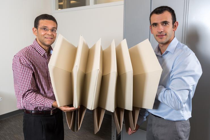 <p>Researchers Glaucio Paulino (left) and Evgueni Filipov show the same large origami structure that has been folded to a much smaller space. Filipov is from University of Illinois at Urbana-Champaign; Paulino is from the Georgia Institute of Technology. (Credit: Rob Felt, Georgia Tech)</p>