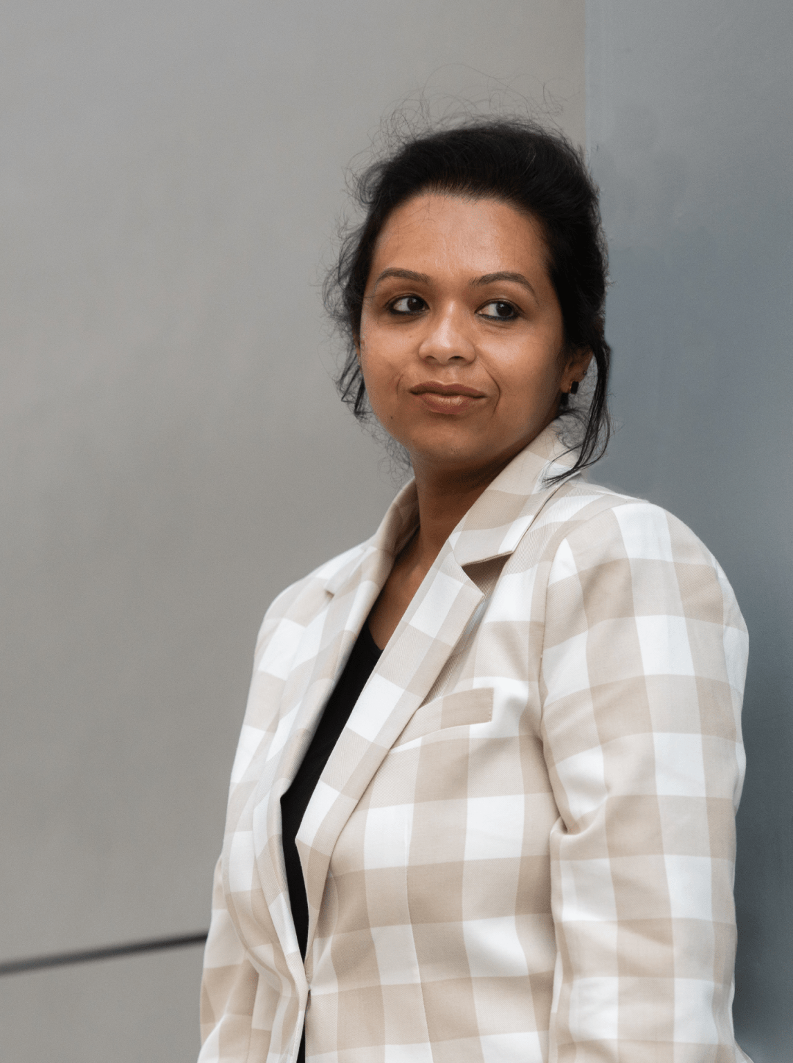 A woman in a beige plaid blazer looks to the right.