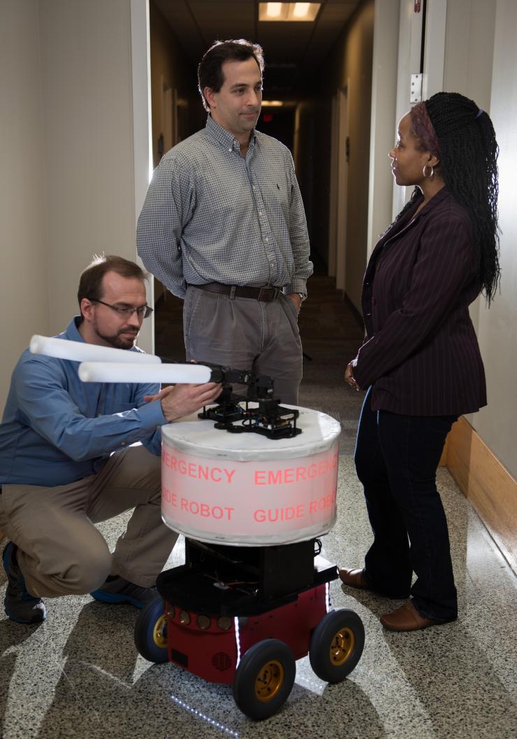 <p>GTRI Research Engineer Paul Robinette adjusts the “arms” on the “Rescue Robot,” while (L-R) GTRI Senior Research Engineer Alan Wagner and School of Electrical and Computer Engineering Professor Ayanna Howard look on. (Credit: Rob Felt, Georgia Tech)</p>